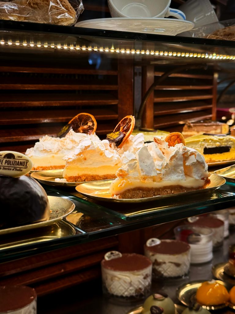 An array of Italian cakes including lemon meringue slices and other desserts in a Tuscan bakery display.